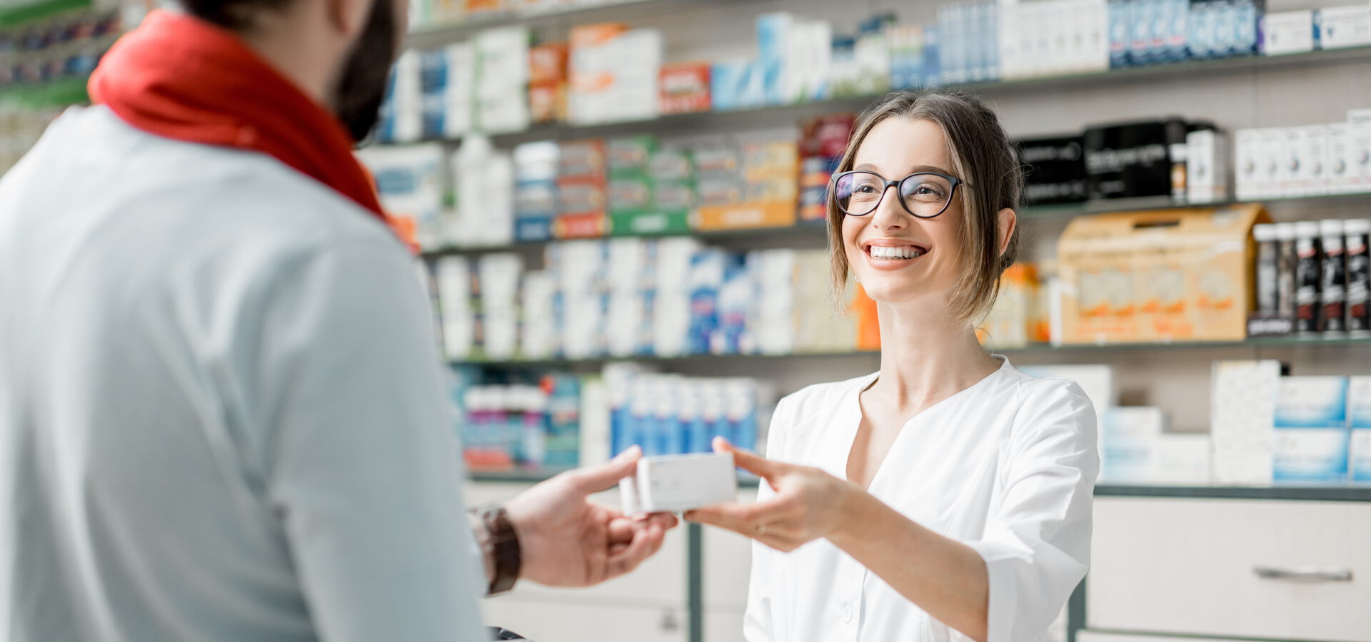 Freundliche Apothekerin reicht Kunden an der Kasse ein Produkt.